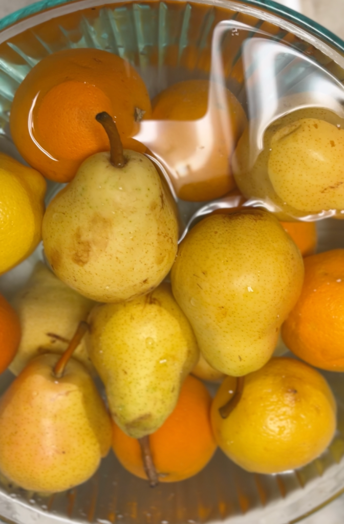 A bowl filled with ripe Bartlett pears, oranges, and a lemon, all soaking in water.